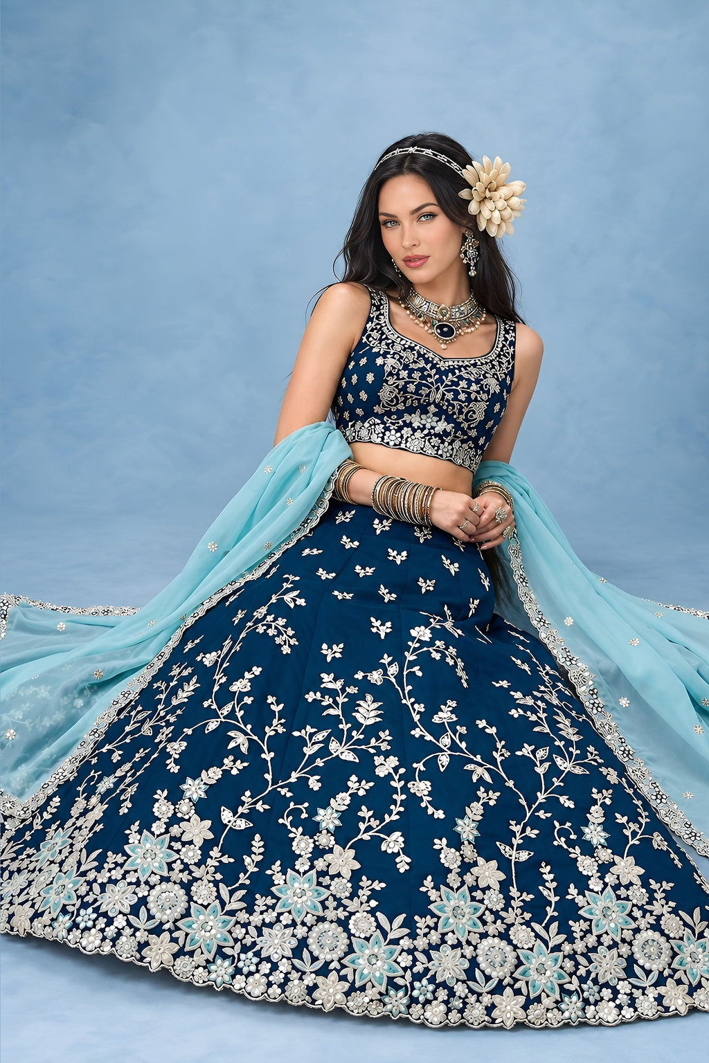 Seated full view of a navy blue lehenga choli for wedding guest, showing the flared rangoli silk skirt and the worked dupatta draped over one arm.