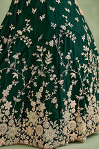 Closeup of the skirt of a dark green lehenga for mehndi, showing the flared rangoli silk fabric and its detailed zari, sequin and thread work.