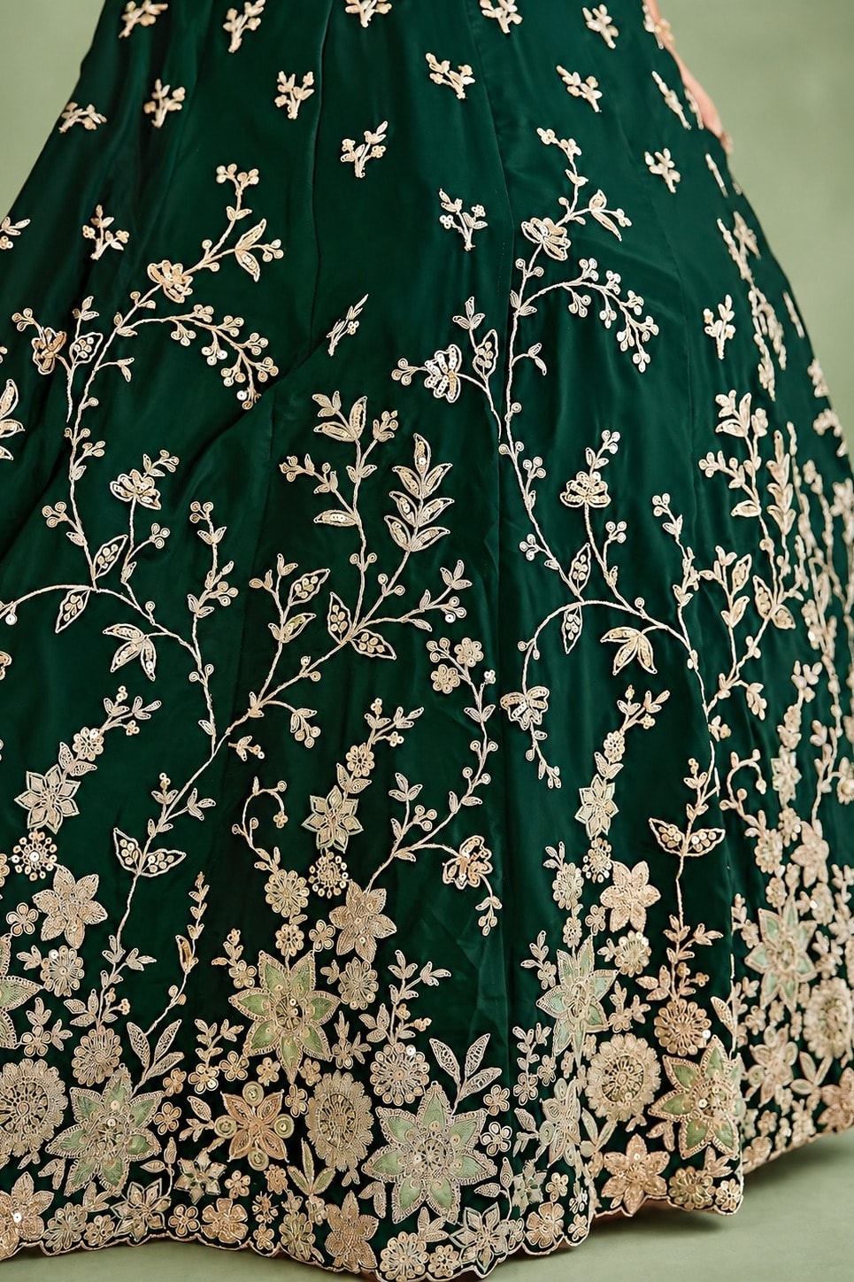 Closeup of the skirt of a dark green lehenga for mehndi, showing the flared rangoli silk fabric and its detailed zari, sequin and thread work.