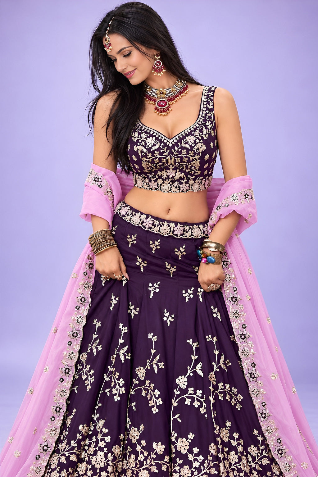 A dark purple lehenga sangeet look in rangoli silk, shown from the front with a flared skirt and a lavender dupatta over one shoulder.