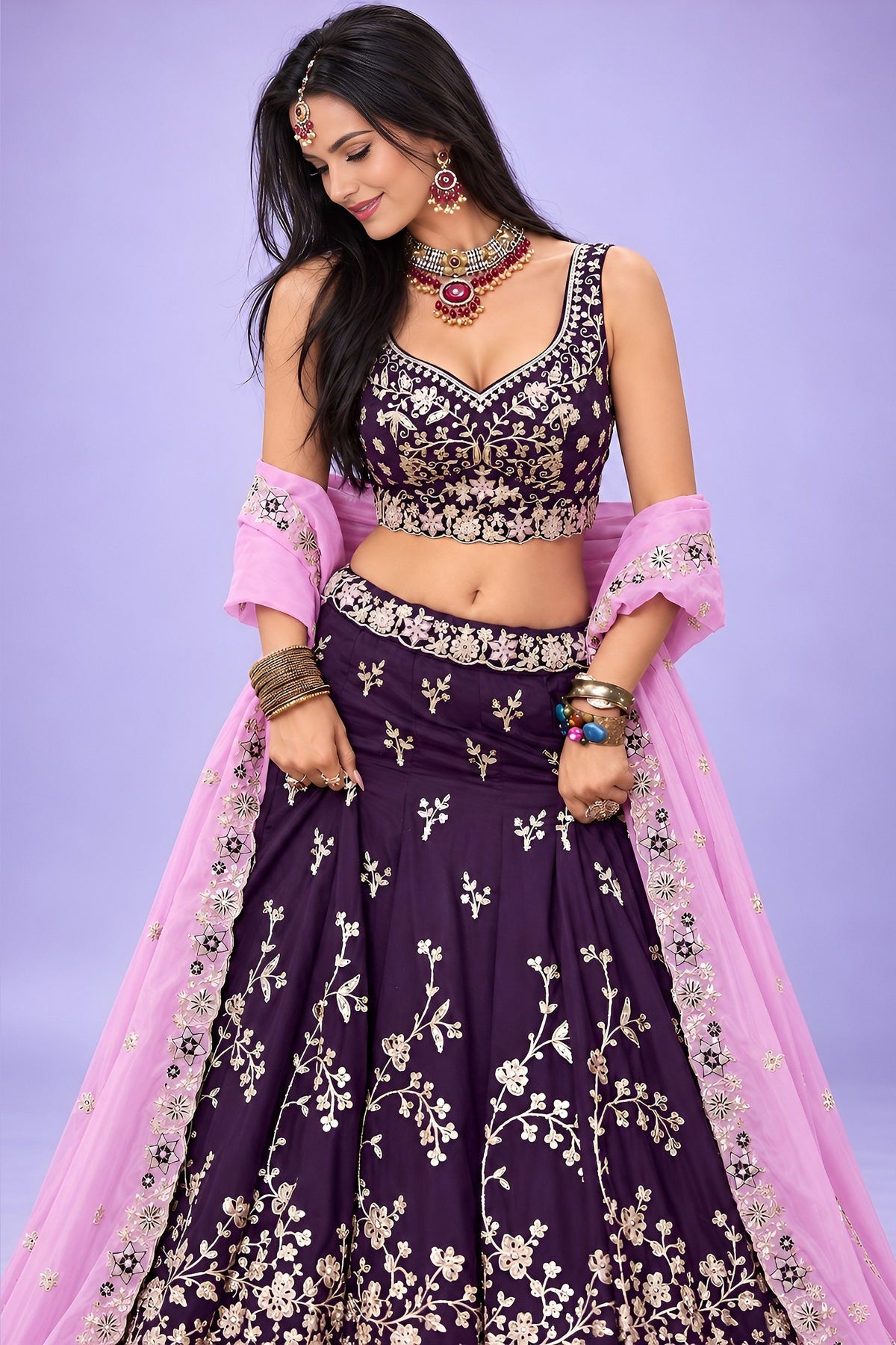 A dark purple lehenga sangeet look in rangoli silk, shown from the front with a flared skirt and a lavender dupatta over one shoulder.