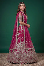 Seated view of a hot pink sangeet lehenga in net with detailed zari, dori and sequins work on the sleeveless blouse and lehenga.