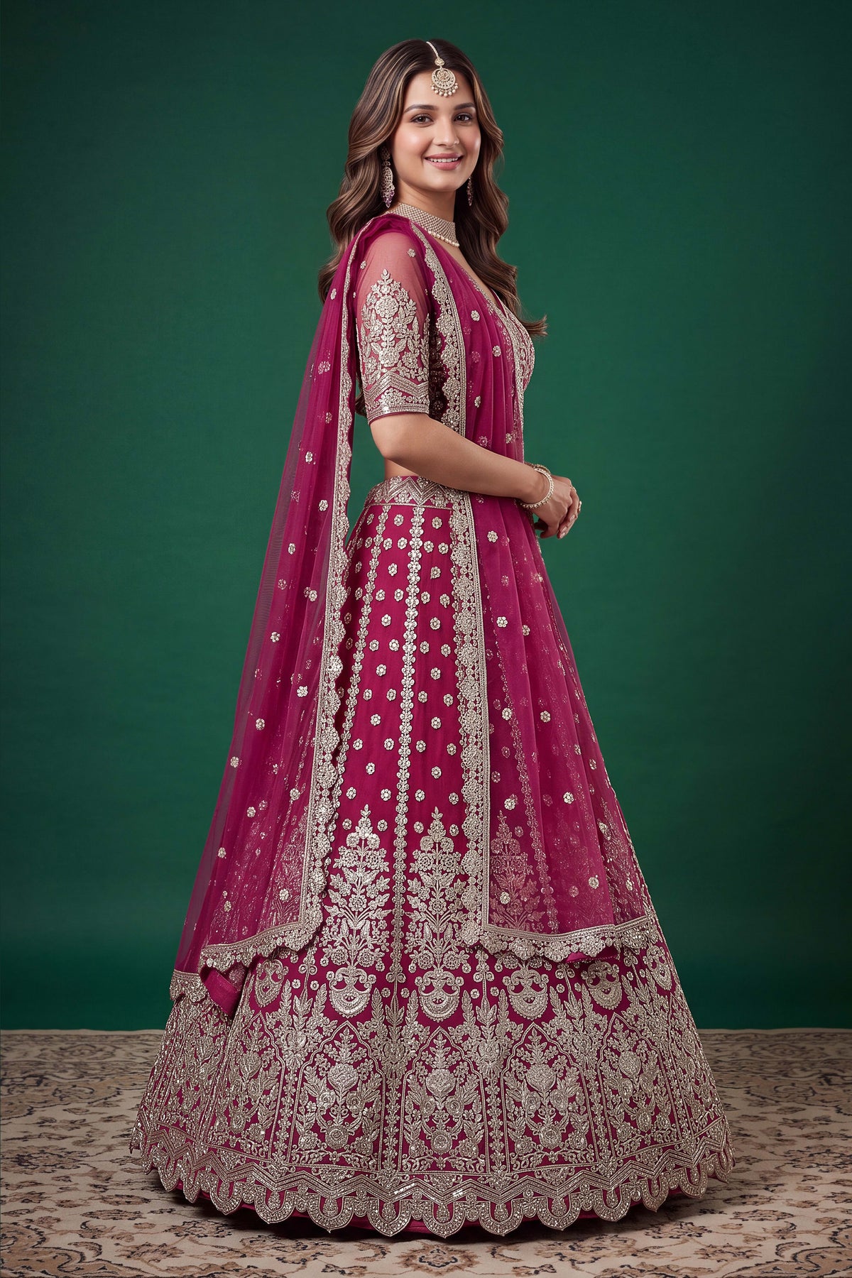 Seated view of a hot pink sangeet lehenga in net with detailed zari, dori and sequins work on the sleeveless blouse and lehenga.