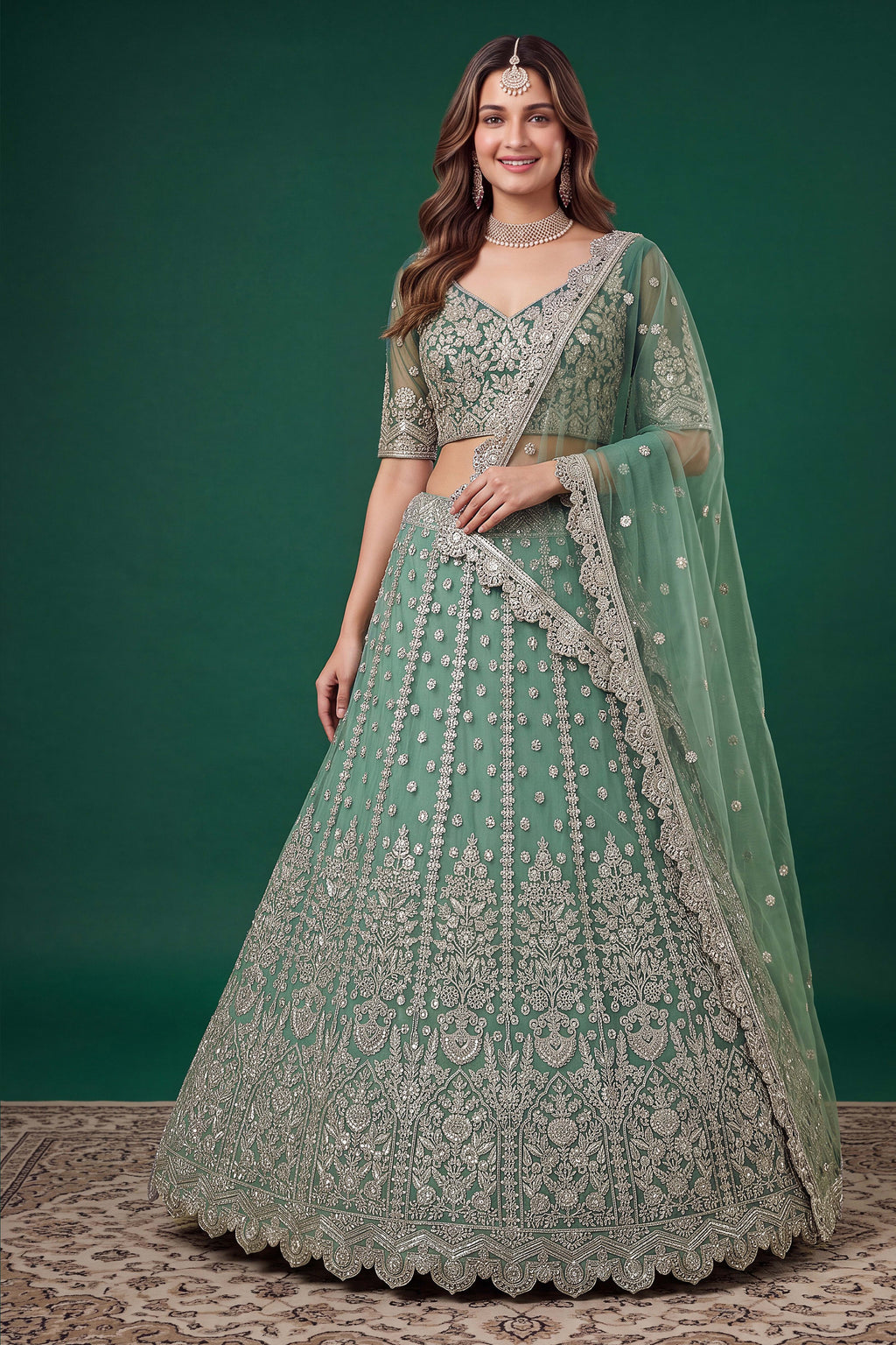 Woman wearing a pista mehndi outfits lehenga in net with zari, dori and sequins work, sleeveless sweetheart blouse, full-length front view.