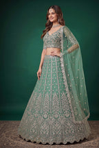 Seated view of a pista party wear lehenga in net with zari, dori and sequins work throughout on the sleeveless blouse and lehenga.
