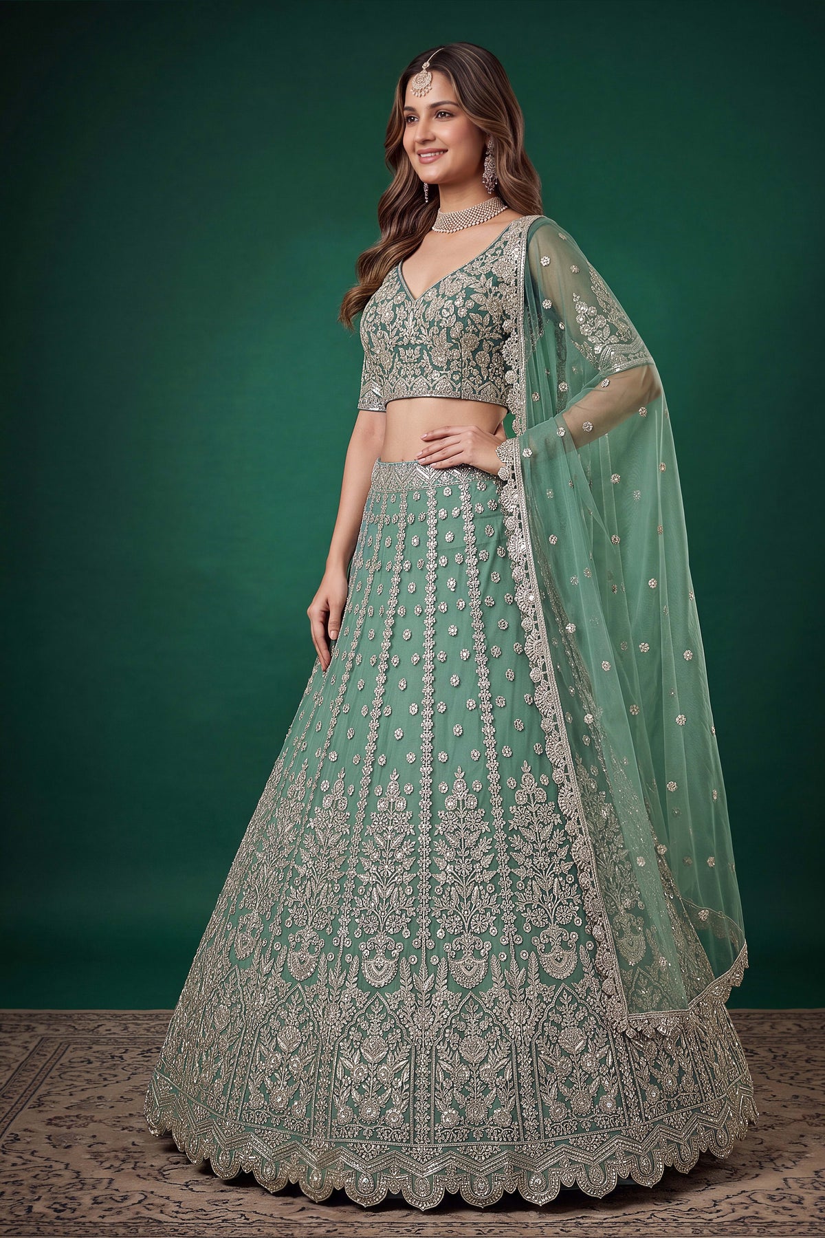 Seated view of a pista party wear lehenga in net with zari, dori and sequins work throughout on the sleeveless blouse and lehenga.