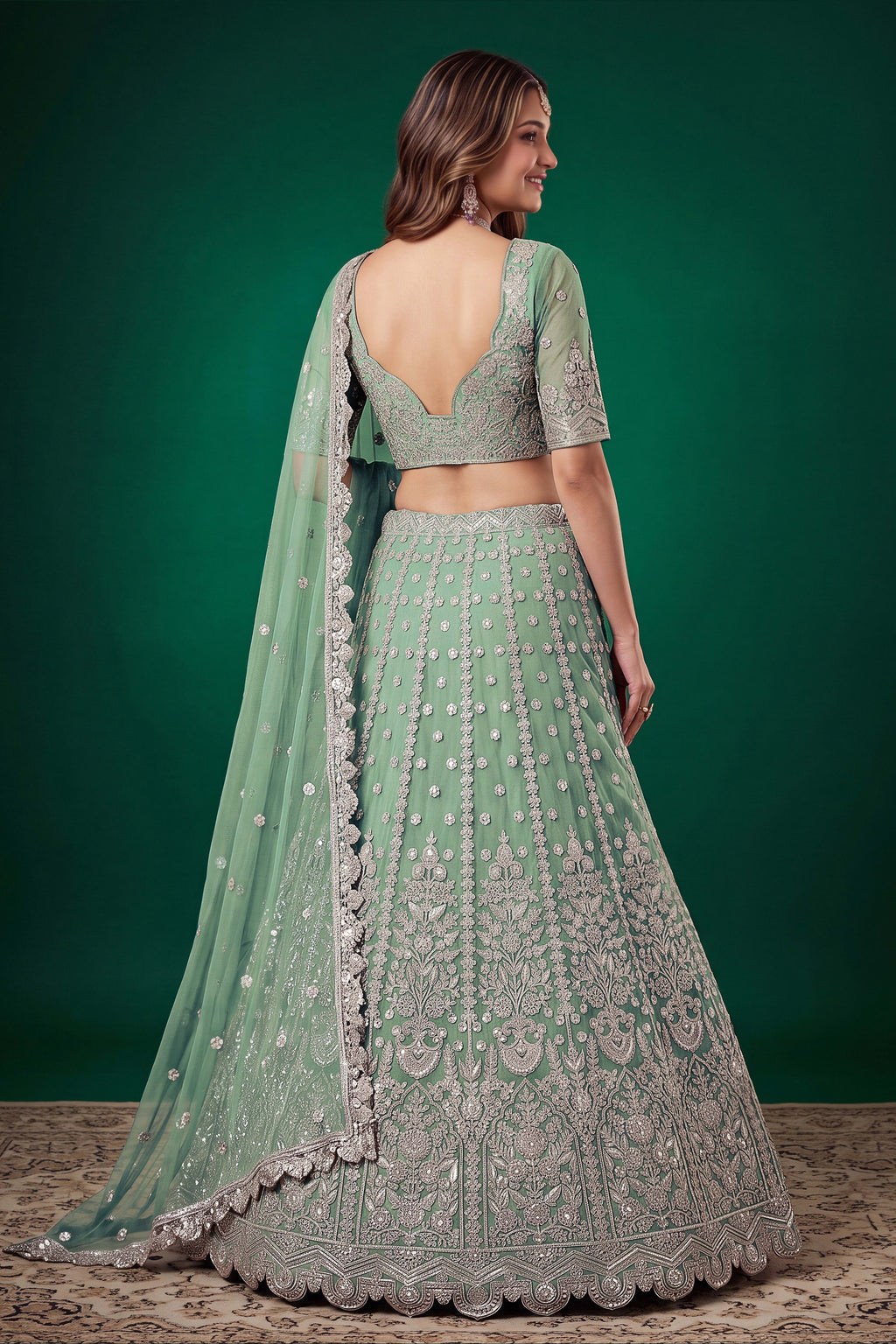 Full-length side view of a pista engagement dresses for women lehenga in net with zari, dori and sequins work on the flared skirt.