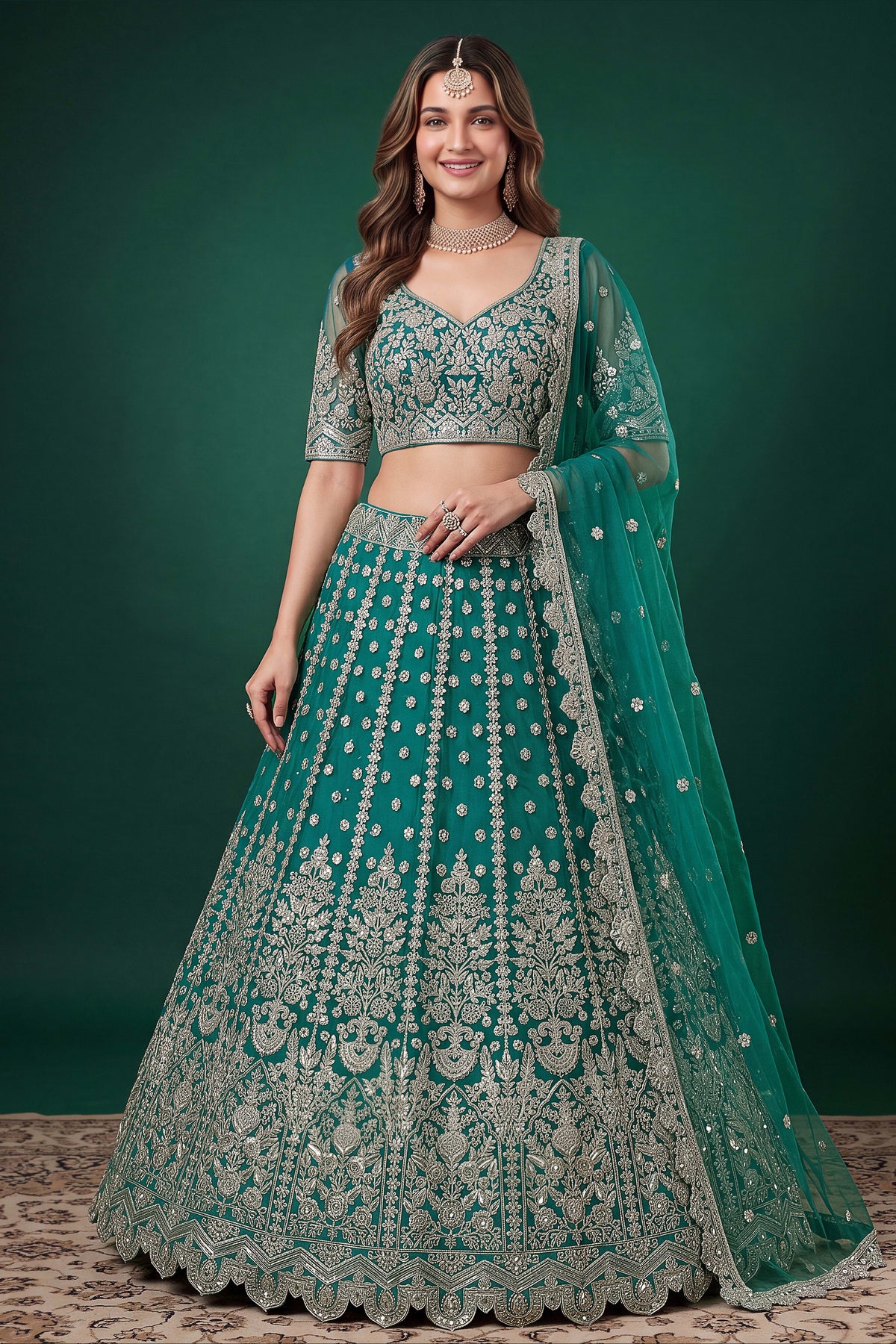 Woman wearing a teal party wear lehenga in net with zari, dori and sequins work, sleeveless sweetheart blouse, full-length front view.