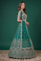 Seated view of a teal cocktail lehenga in net with zari, dori and sequins work throughout on the sleeveless blouse and lehenga.