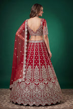 Seated view of a red engagement lehenga in net with zari, dori and sequins work throughout on the sleeveless blouse and lehenga.