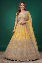 Woman wearing a mustard yellow haldi outfits lehenga in net with zari, dori and sequins work, sleeveless blouse, full-length front view.