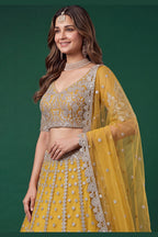 Seated view of a mustard yellow cocktail lehenga in net with zari, dori and sequins work on the sleeveless blouse and lehenga.