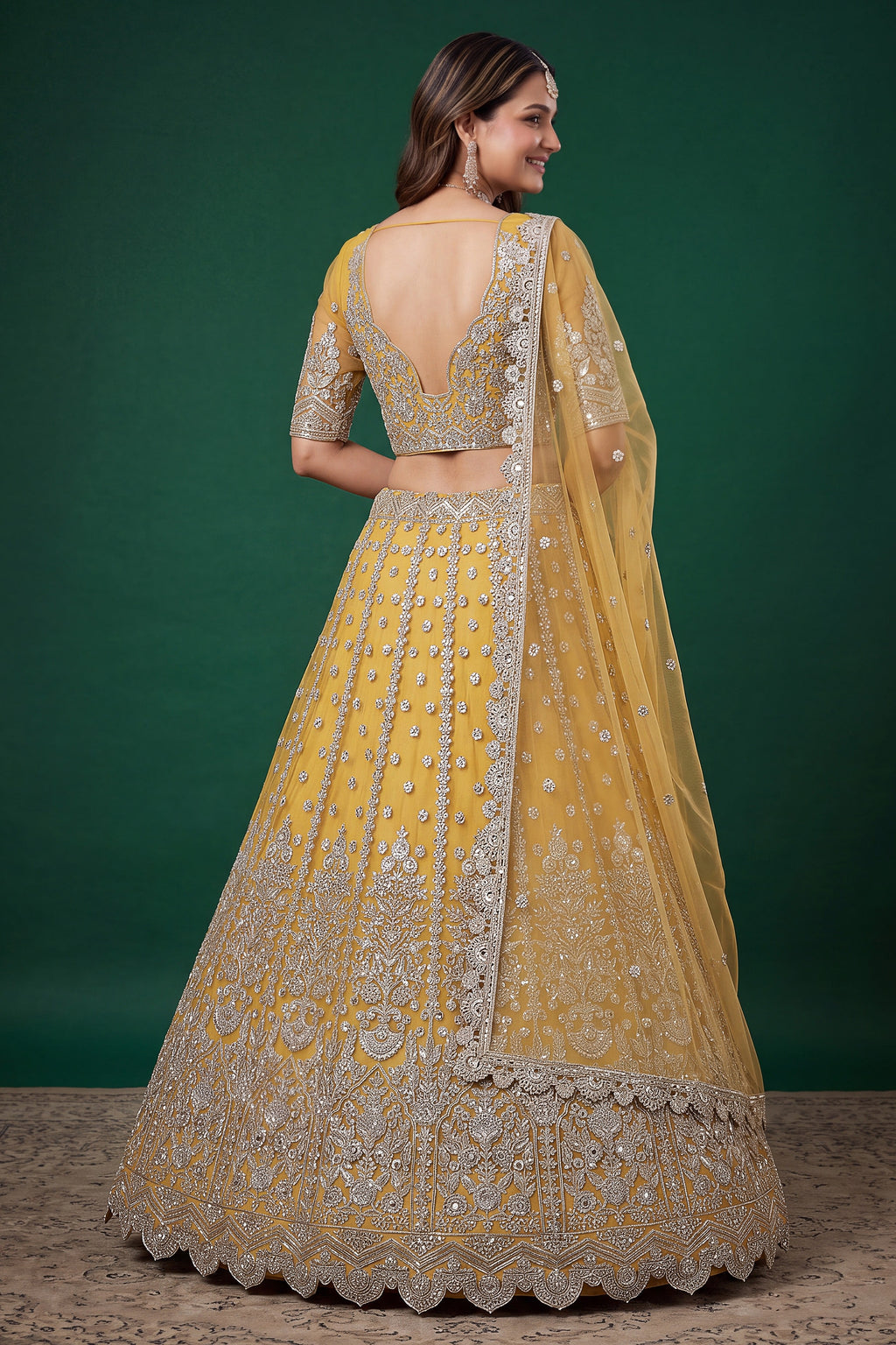 Full-length side view of a mustard yellow engagement dresses for women lehenga in net with zari, dori and sequins work on the flared skirt.
