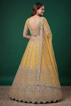 Full-length side view of a mustard yellow engagement dresses for women lehenga in net with zari, dori and sequins work on the flared skirt.