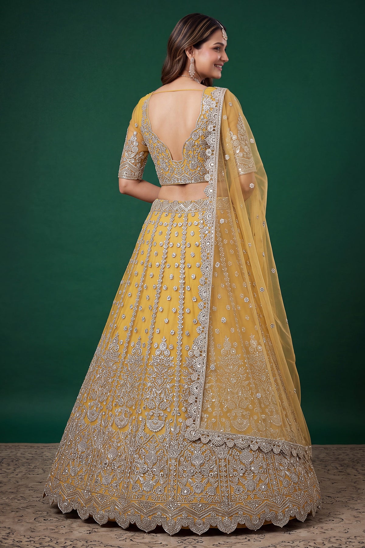 Full-length side view of a mustard yellow engagement dresses for women lehenga in net with zari, dori and sequins work on the flared skirt.