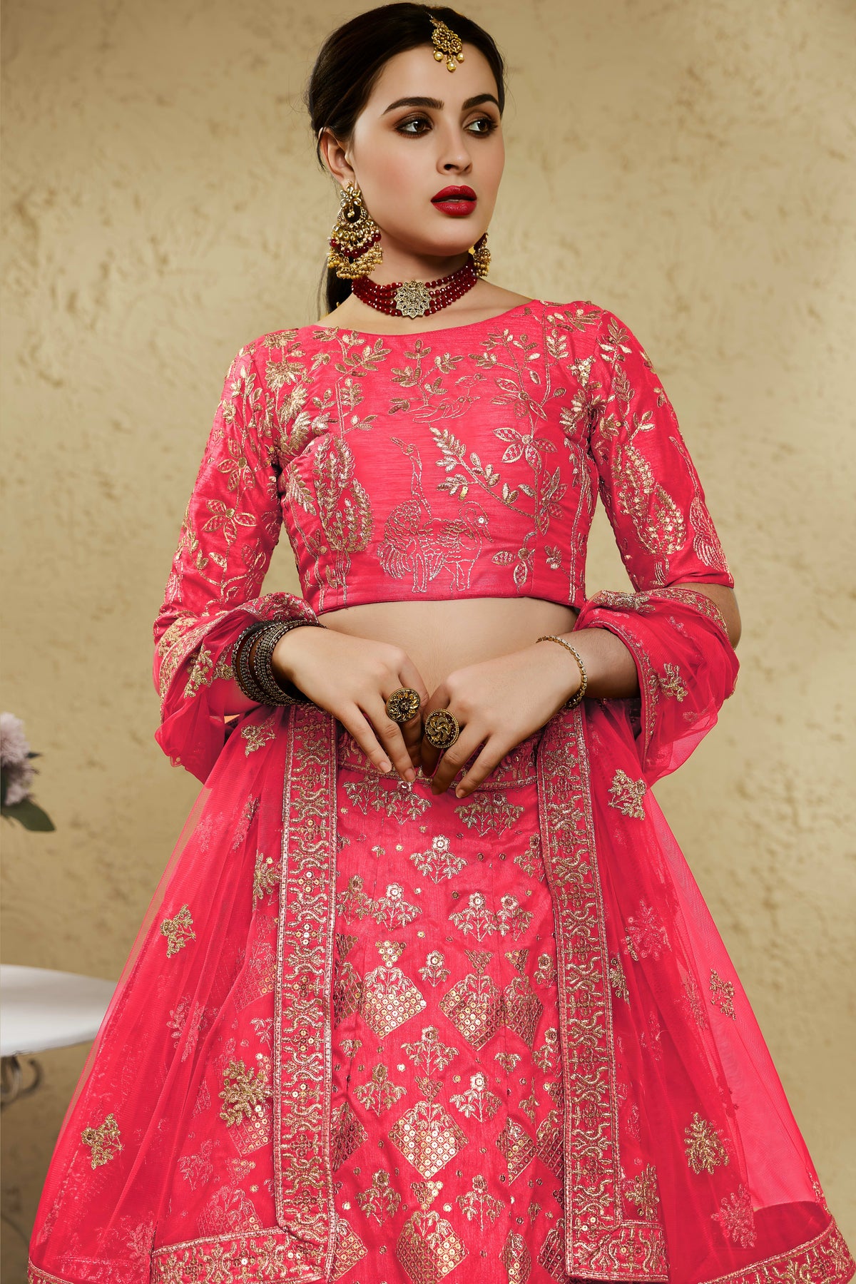 Close-up view of a pinkish red lehenga for wedding in art silk with detailed zari and sequin embroidery work on the blouse and lehenga skirt.