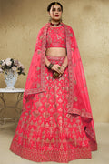 Woman wearing a pinkish red lehenga for wedding in art silk with zari and sequin embroidery, half sleeve boat neck blouse, full-length front view.