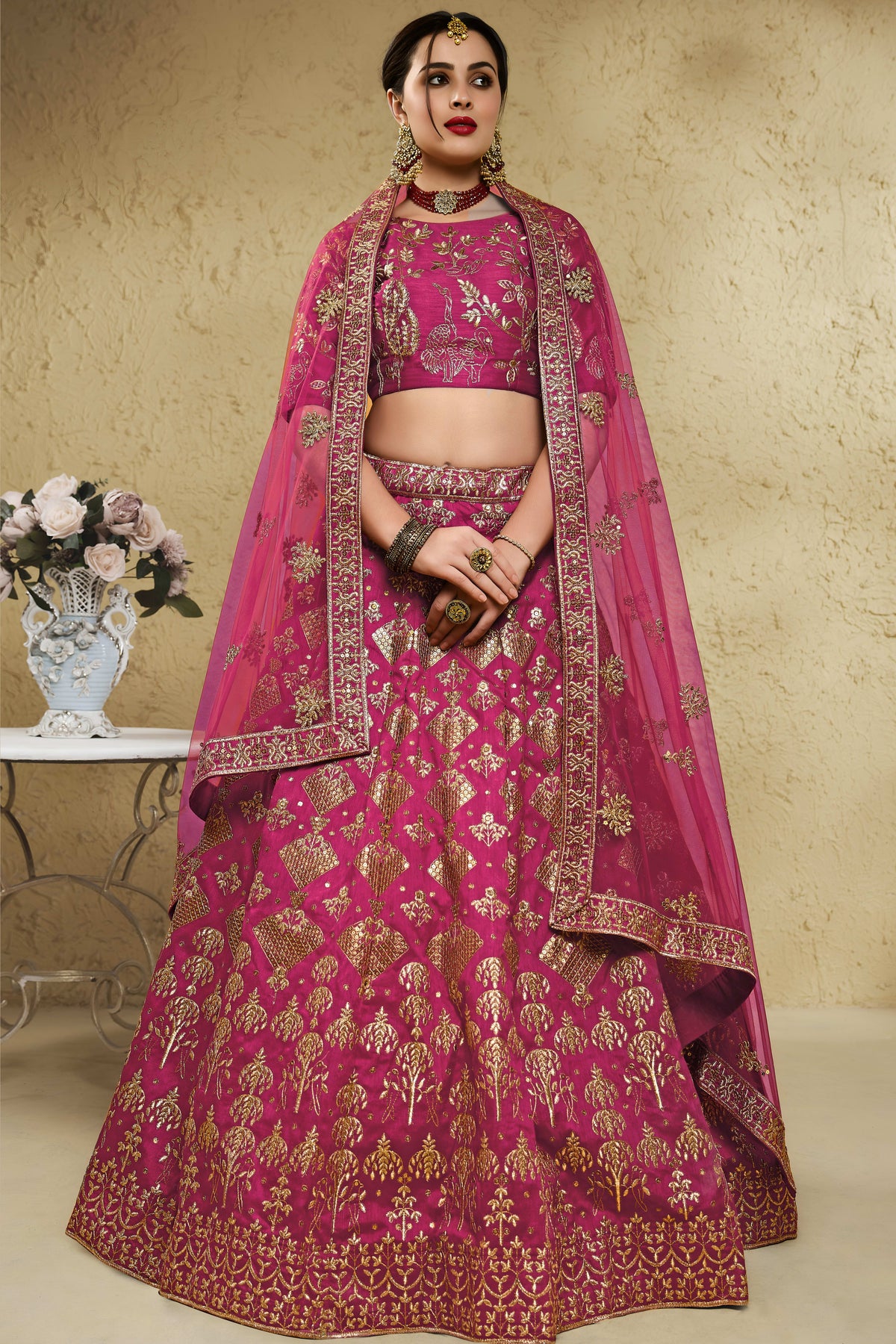 Woman wearing a dark pink reception lehenga in art silk with zari and sequin embroidery, half sleeve boat neck blouse, full-length front view.