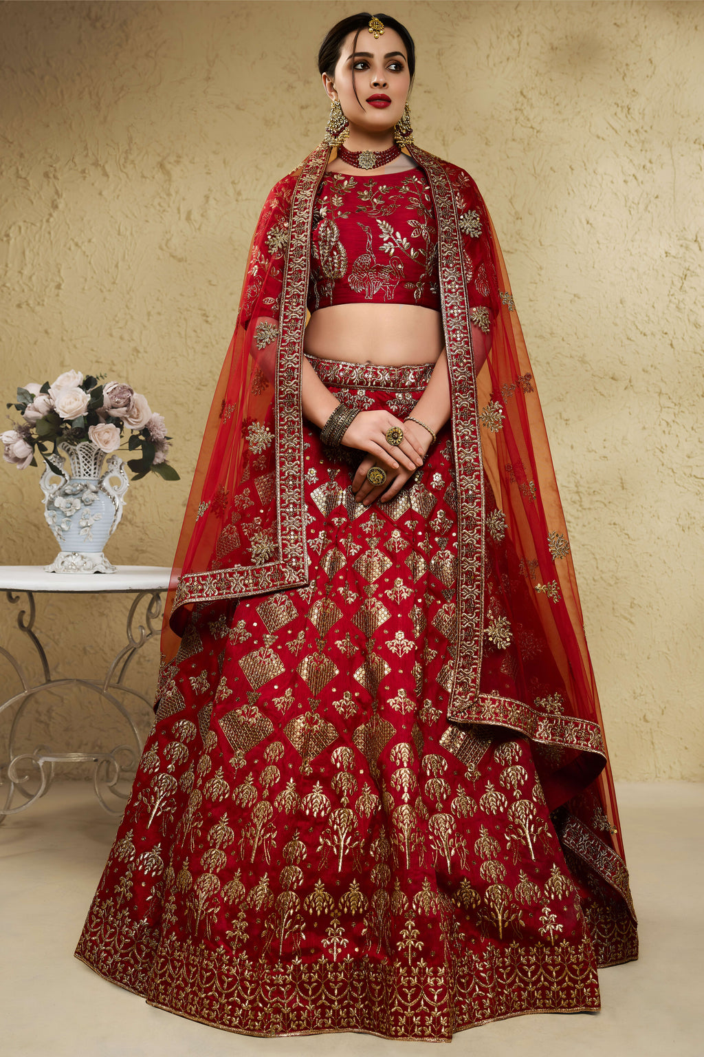 Woman wearing a red engagement lehenga in art silk with zari and sequin embroidery, half sleeve boat neck blouse, full-length front view.