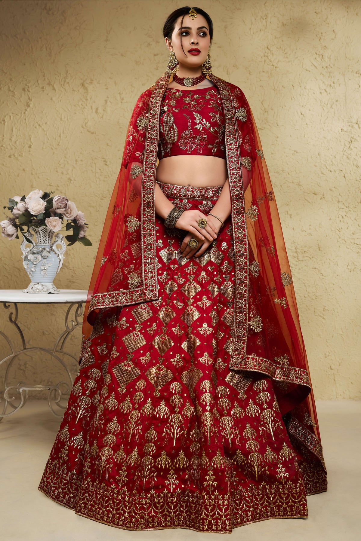 Woman wearing a red engagement lehenga in art silk with zari and sequin embroidery, half sleeve boat neck blouse, full-length front view.