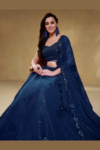 Seated view of a blue engagement lehenga in georgette with zari, dori and sequin work on the sleeveless blouse and lehenga.