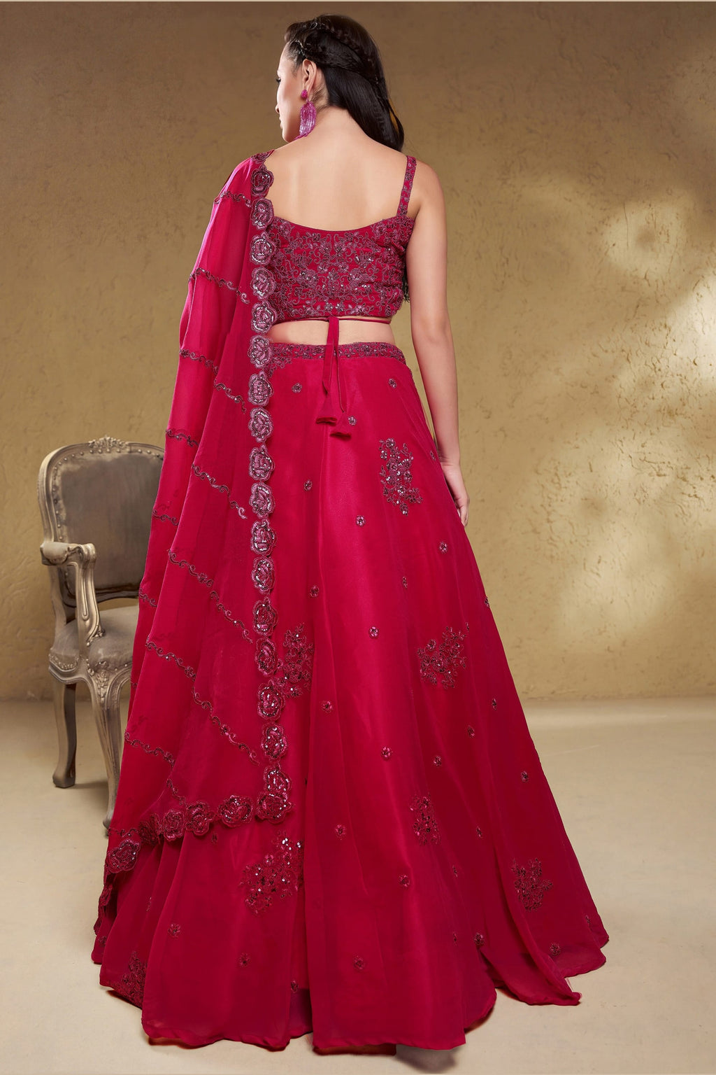 Full-length back view of a reddish pink reception lehenga in georgette with an open back blouse with dori tie and zari and sequin work.