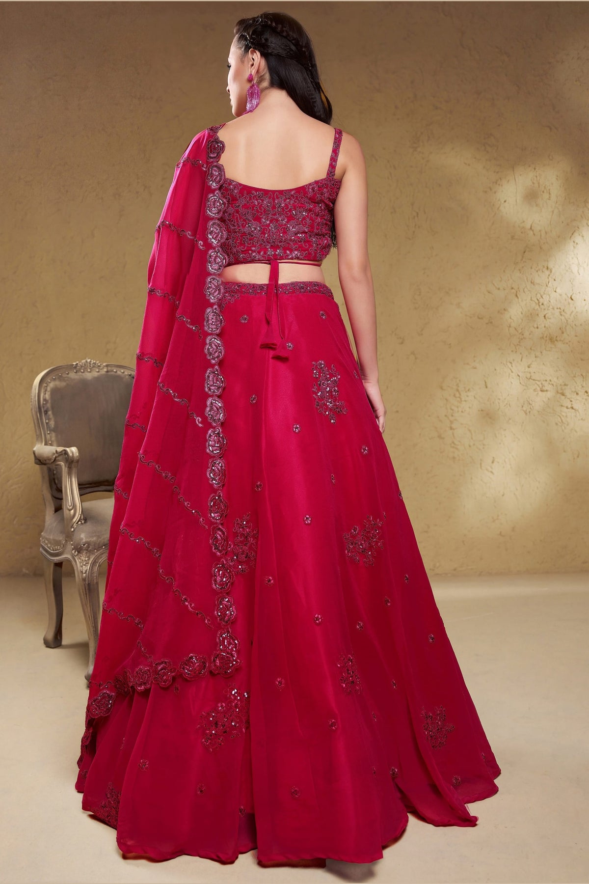 Full-length back view of a reddish pink reception lehenga in georgette with an open back blouse with dori tie and zari and sequin work.