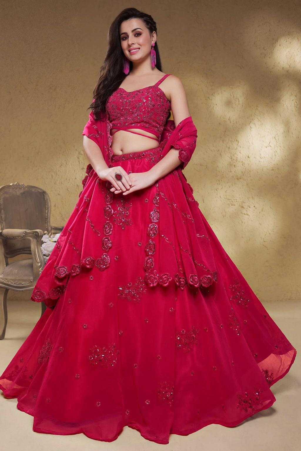 Woman wearing a reddish pink reception lehenga in georgette with zari, dori and sequin work, sleeveless sweetheart blouse, full-length front view.