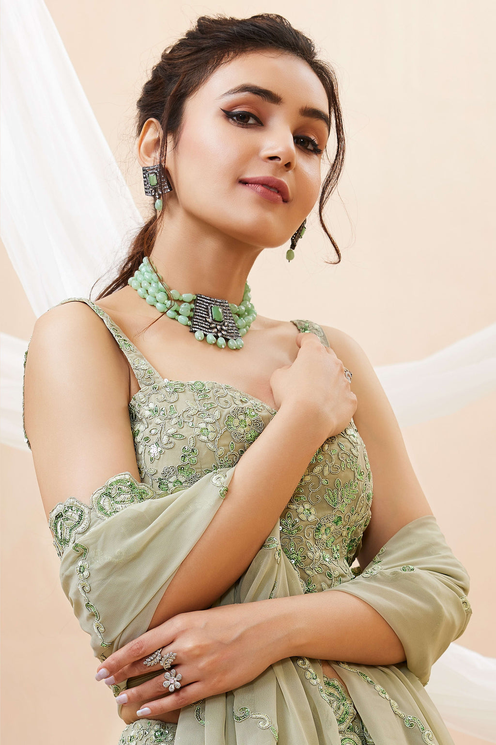 Seated view of a pista green party wear lehenga in georgette with zari, dori and sequin work on the sleeveless blouse and lehenga.