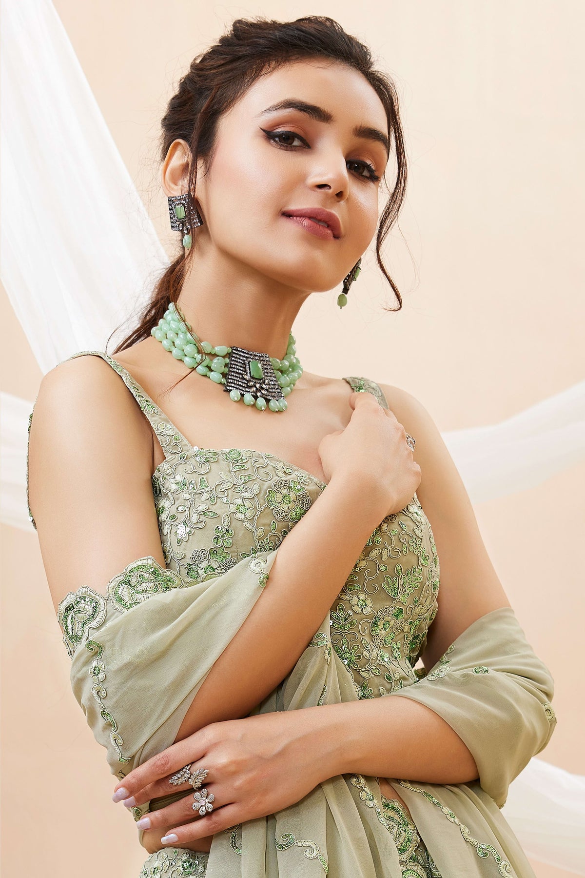 Seated view of a pista green party wear lehenga in georgette with zari, dori and sequin work on the sleeveless blouse and lehenga.