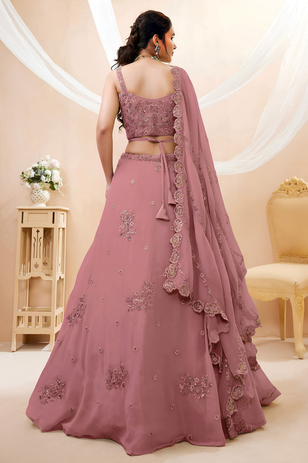 Full-length back view of a rust pink lehenga for wedding in georgette with an open back blouse with dori tie and zari and sequin work.