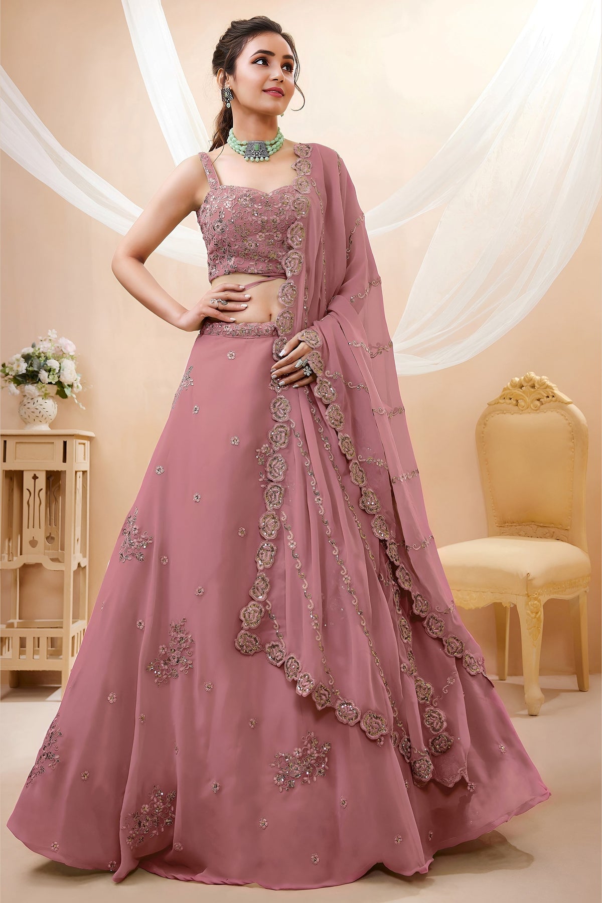 Woman wearing a rust pink lehenga for wedding in georgette with zari, dori and sequin work, sleeveless sweetheart blouse, full-length front view.
