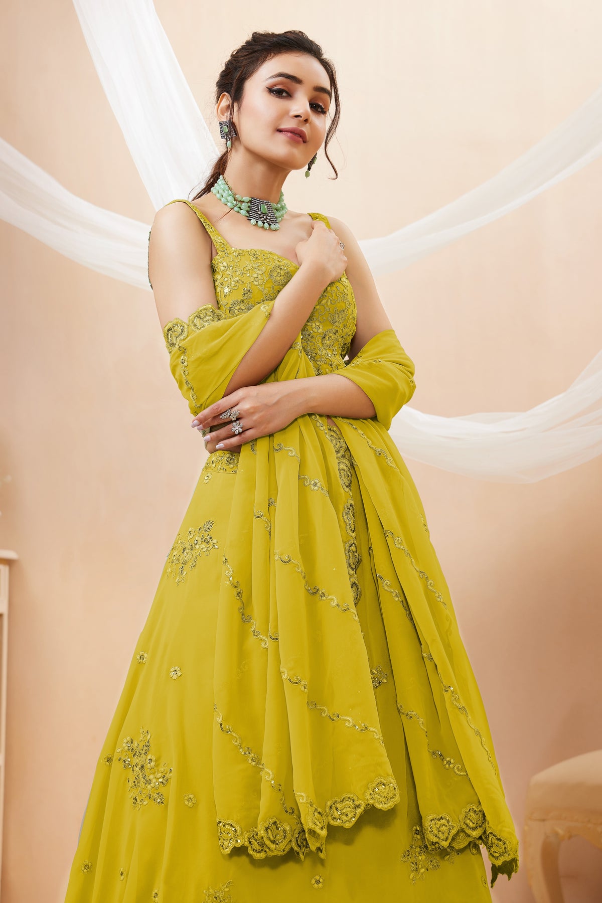 Seated view of a bright yellow engagement dresses for women lehenga in georgette with zari, dori and sequin work on the sleeveless blouse and lehenga.