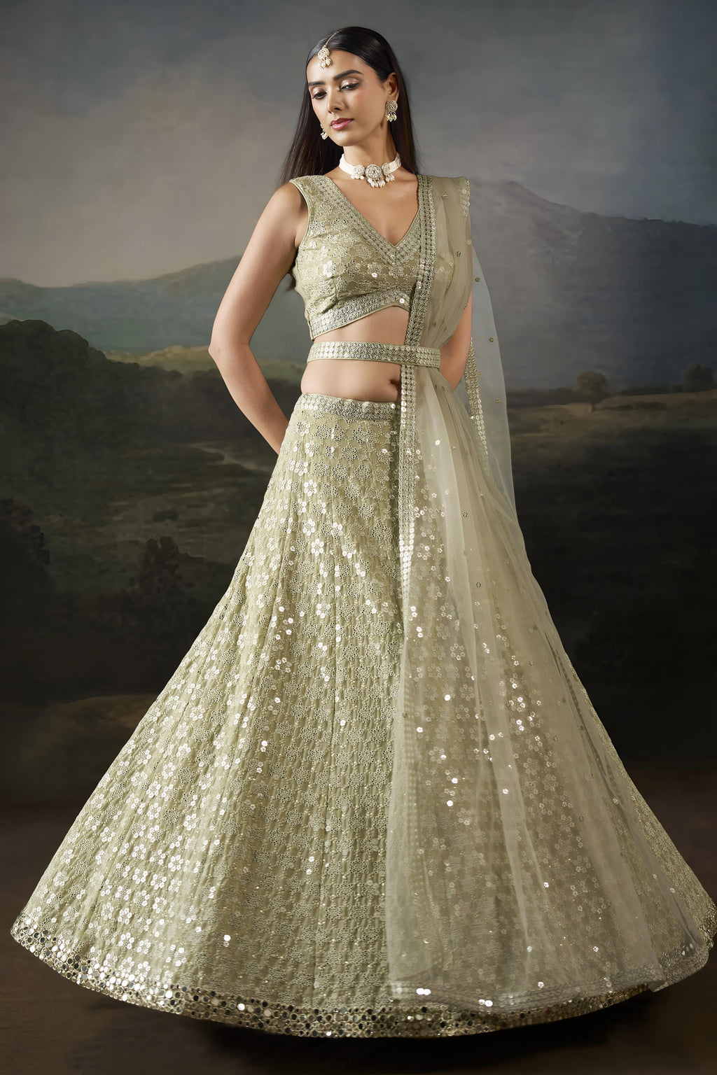 Full front view of the champagne mehndi lehenga with a sleeveless V neck blouse, worked belt and net dupatta falling to the side.