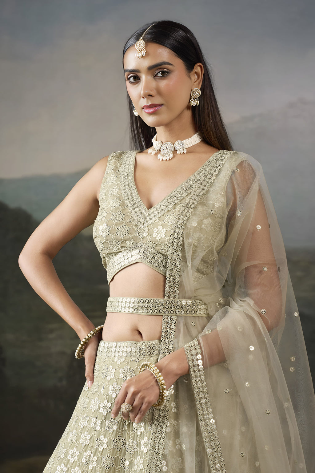 Half view of the champagne mehendi lehenga with a sleeveless V neck blouse, sequin work and a sheer net dupatta over the shoulder.