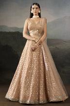 Model wearing a pale peach sangeet lehenga with a sleeveless V neck blouse, worked belt and sheer net dupatta, standing in a full front pose.