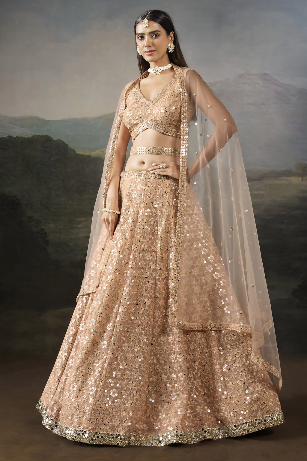 Front view of the pale peach lehenga, a graceful sangeet outfits for women option, with a V neck blouse and net dupatta falling to the side.