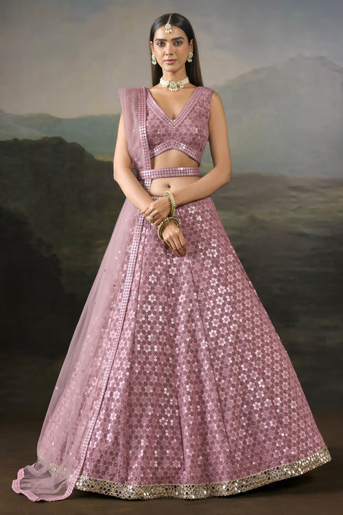 Model wearing a baby pink sangeet lehengas set with a sleeveless V neck blouse, worked belt and sheer net dupatta, standing front-facing.