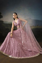 Seated pose of the baby pink sangeet attire with the flared sequinned lehenga spread out and the net dupatta draped to the side.