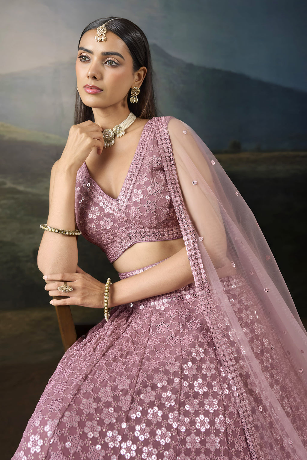 Half view of the baby pink wedding wear lehenga choli with a sleeveless V neck blouse, sequin work and a sheer net dupatta.