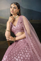 Half view of the baby pink wedding wear lehenga choli with a sleeveless V neck blouse, sequin work and a sheer net dupatta.