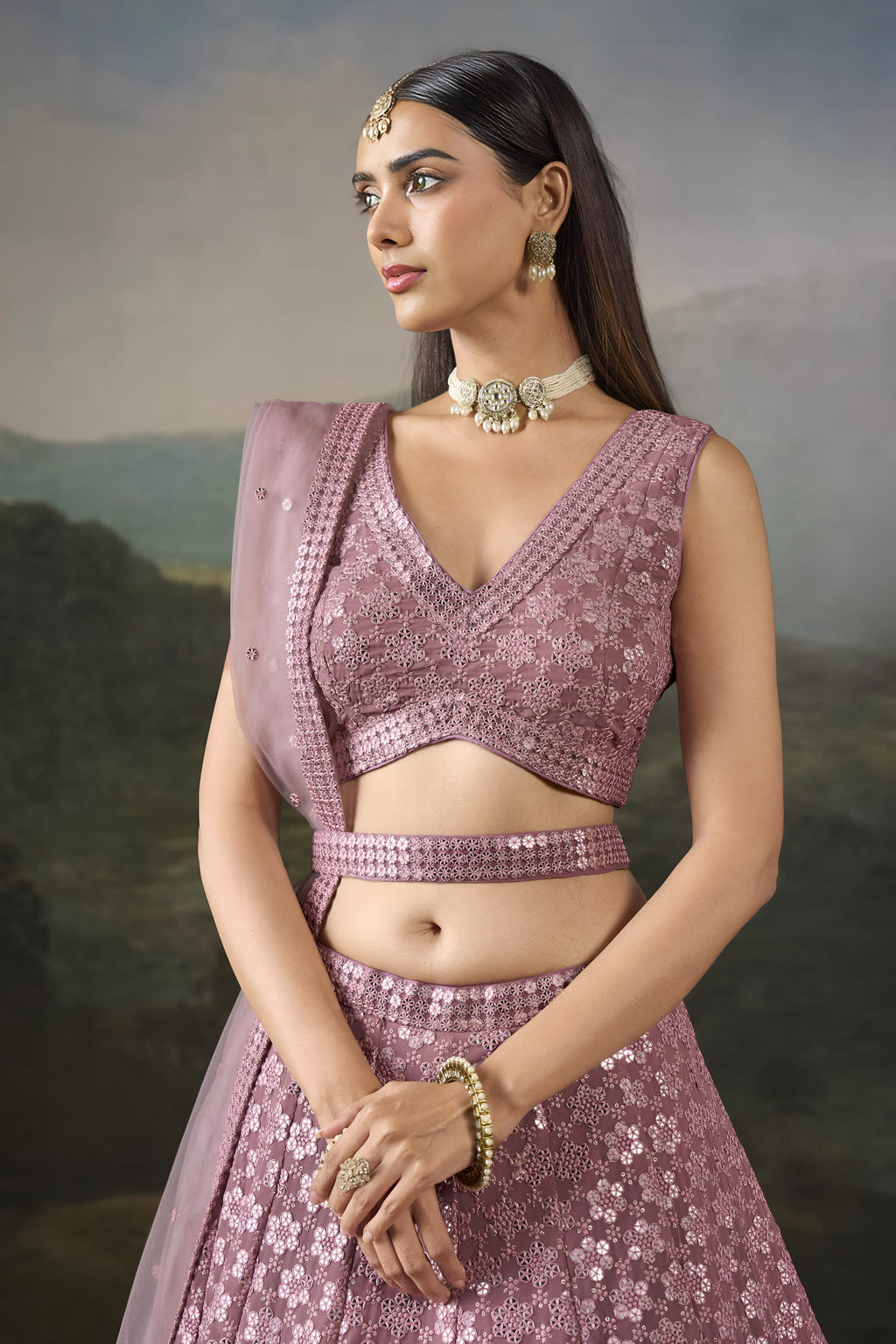 Half view of the baby pink wedding wear lehenga choli showing the V neck blouse, mirror work and sheer net dupatta over one shoulder.