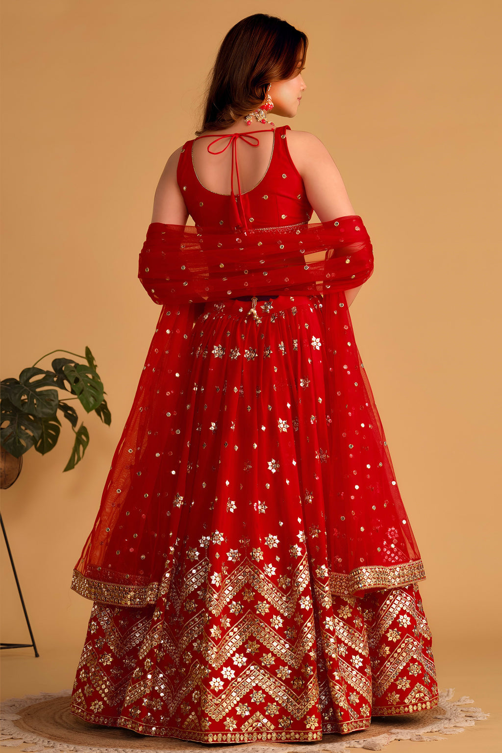 Full-length back view of a red lehenga for wedding with an open back choli with dori tie and zari and sequin embroidery.