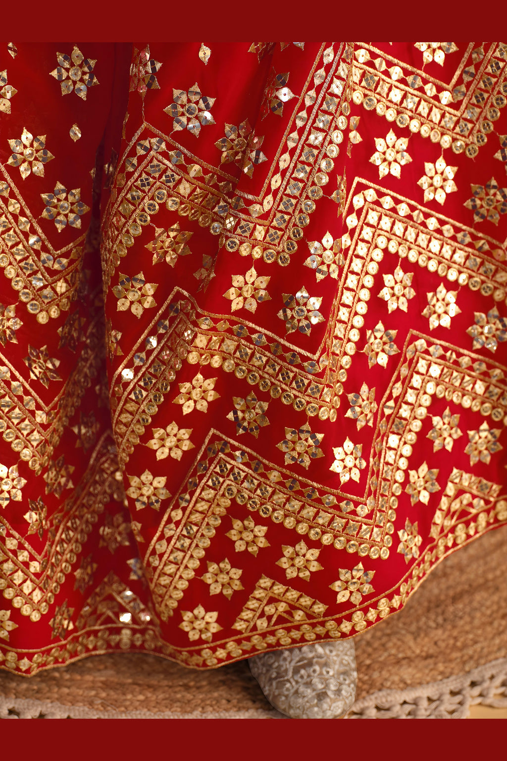 Detail view of a red reception lehenga showing intricate zari and sequin embroidery throughout on the lehenga skirt border.