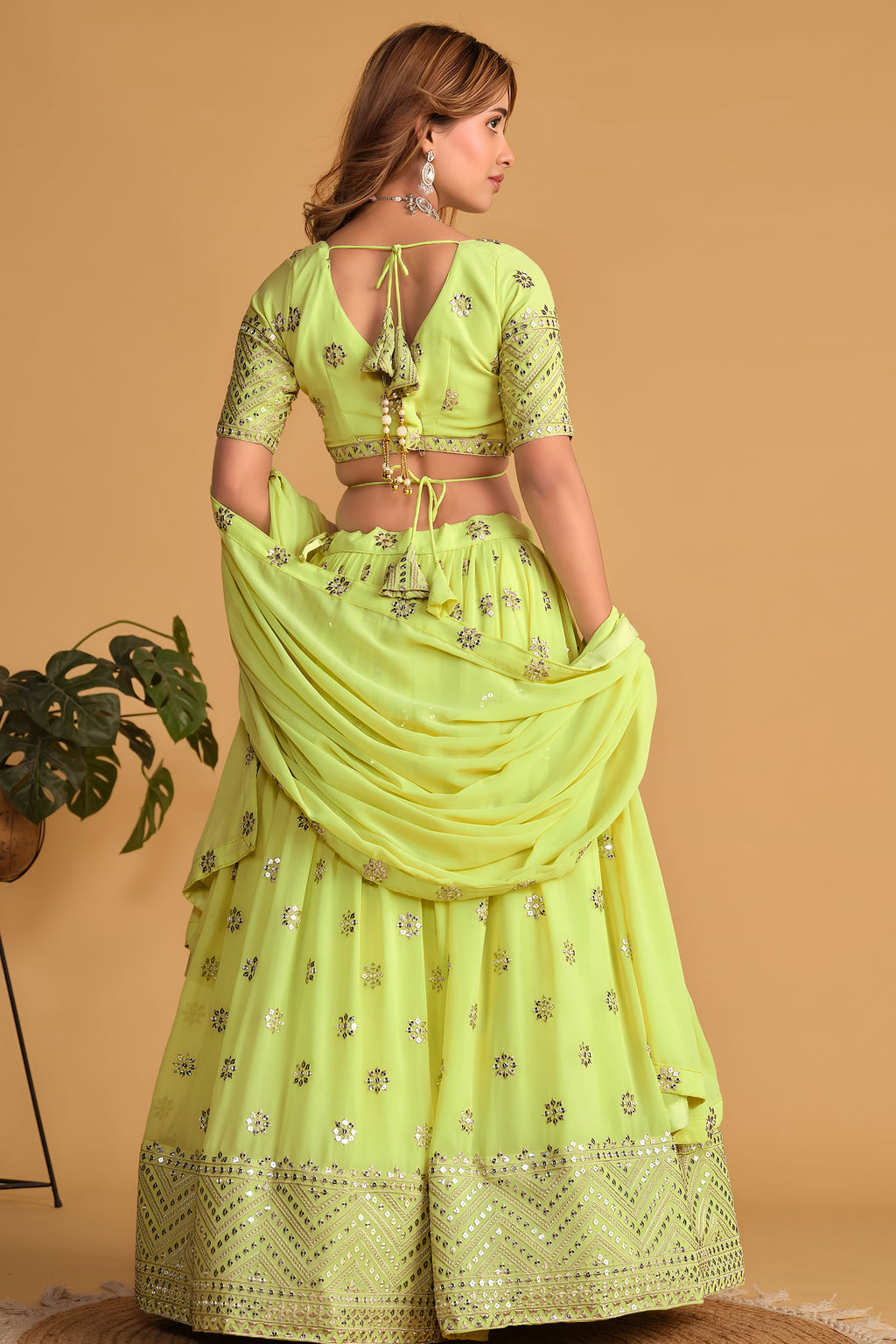 Full-length back view of a neon yellow party wear lehenga with V neckline back choli and zari and sequin embroidery work.