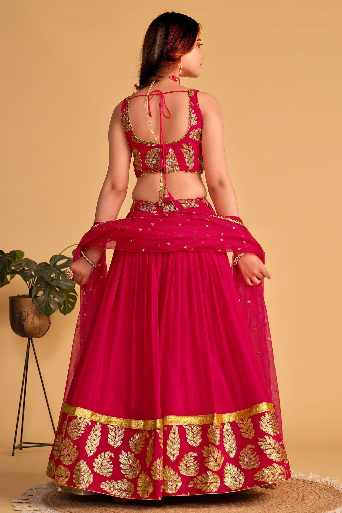 Full-length back view of a reddish pink sangeet lehenga with deep neckline back choli and zari and sequin embroidery work.