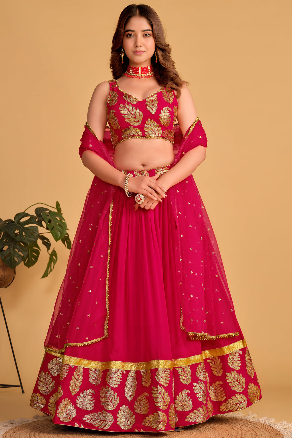 Woman wearing a reddish pink sangeet lehenga with zari and sequin embroidery, sleeveless sweetheart neck choli, full-length front view.