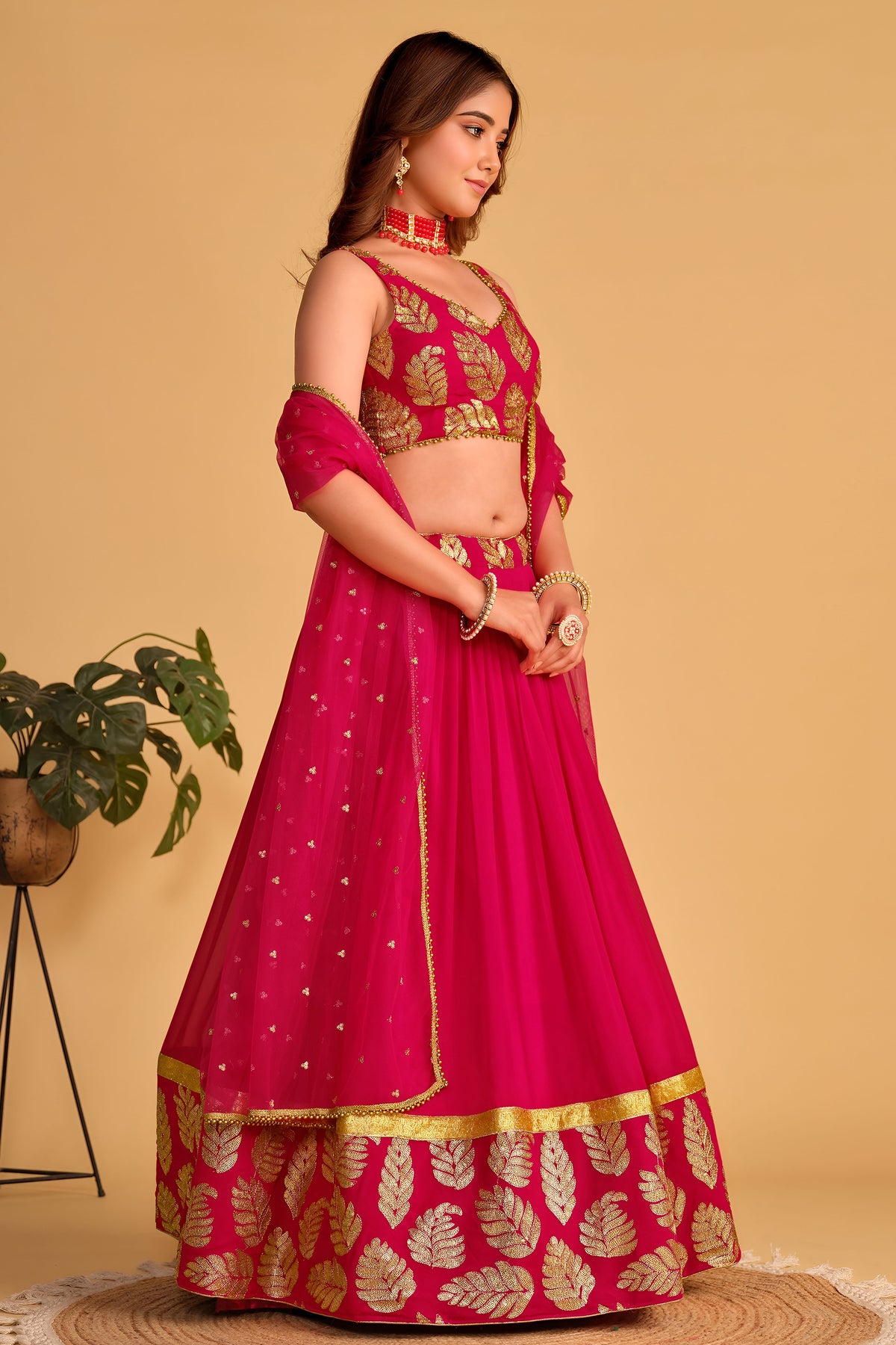 Full-length side view of a reddish pink sangeet lehenga with zari and sequin embroidery throughout on the flared lehenga skirt.