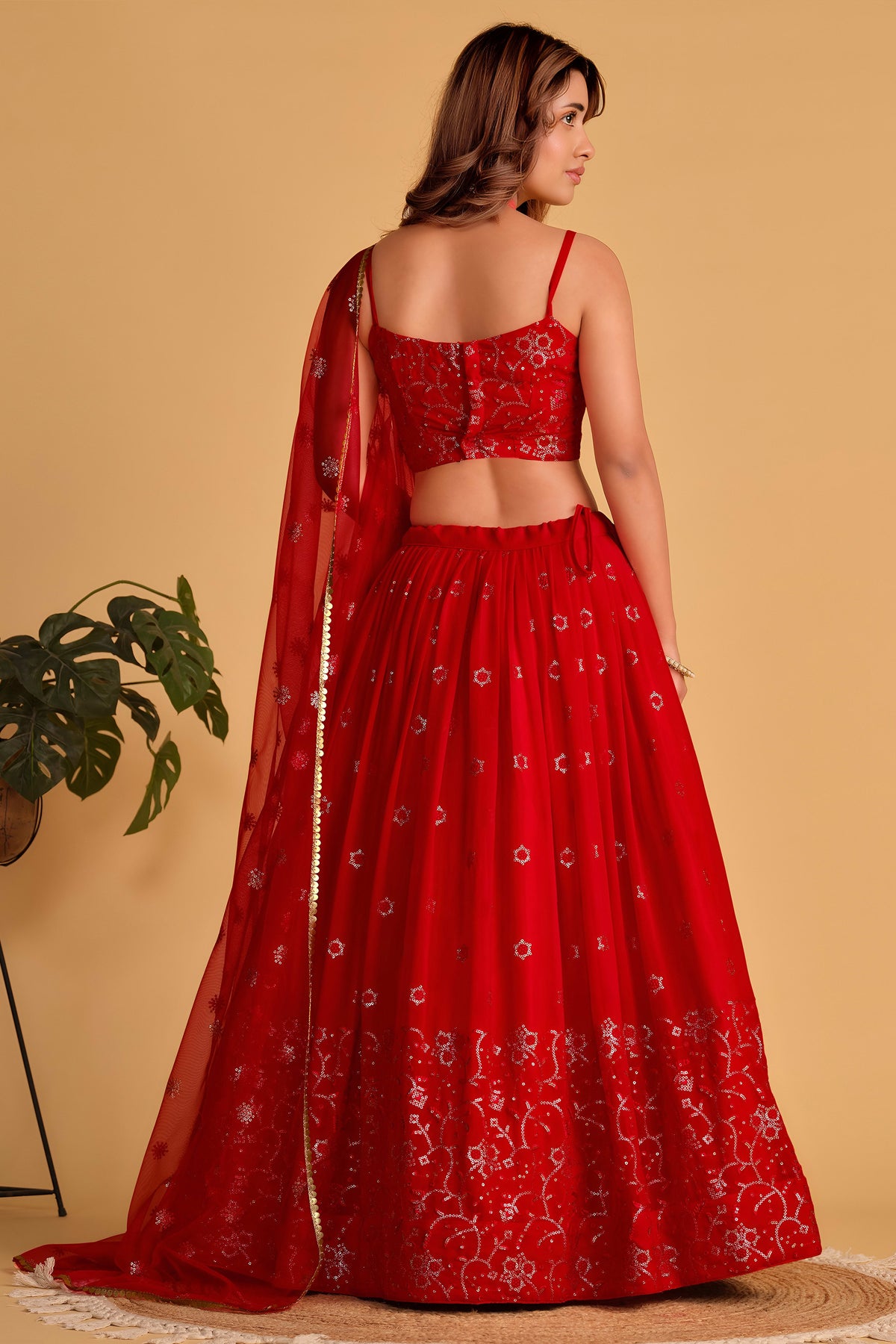 Full-length side view of a reddish pink engagement lehenga with zari and sequin embroidery throughout on the flared lehenga skirt.