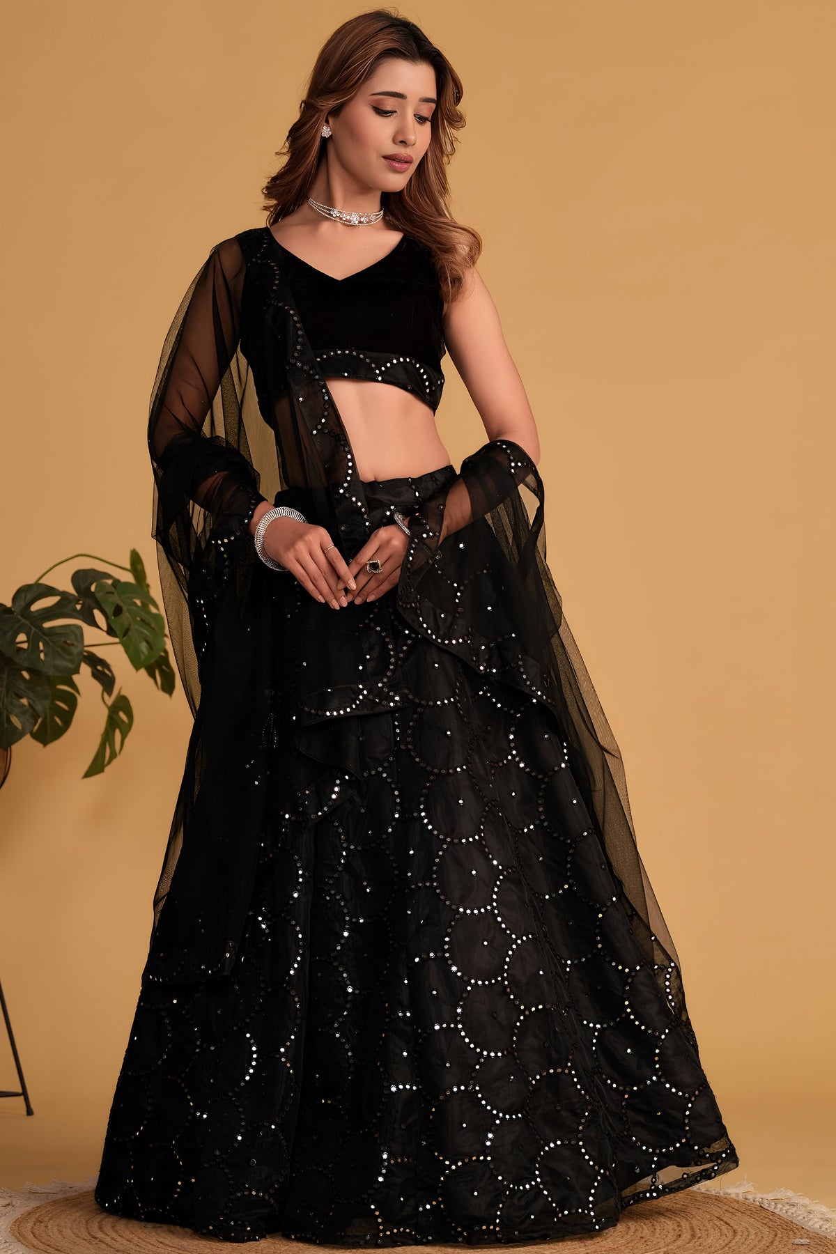 Woman wearing a black cocktail lehenga with zari and sequin embroidery, sleeveless V neck velvet choli, full-length front view.